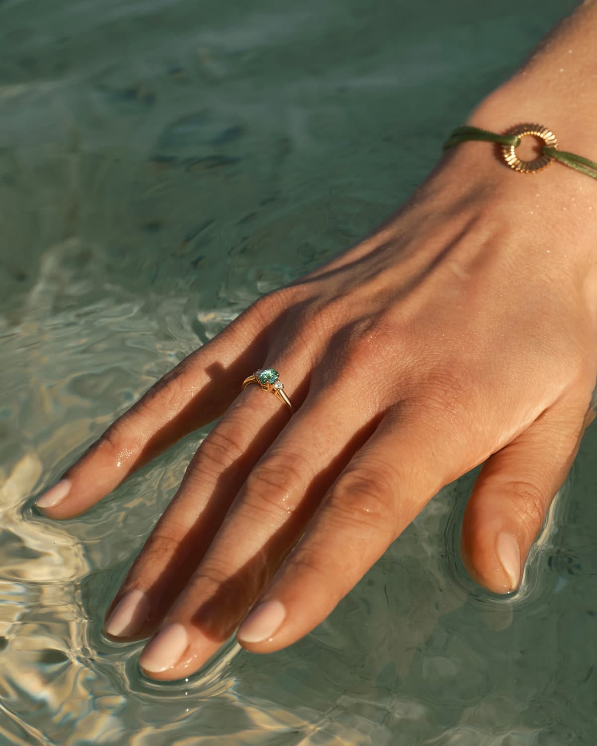 Hand eines Models, das den Baby Lady Duo Oval Ring aus Roségold und Turmalin Mint und das olivgrüne Entaille Rayons Kordelarmband aus Roségold trägt.